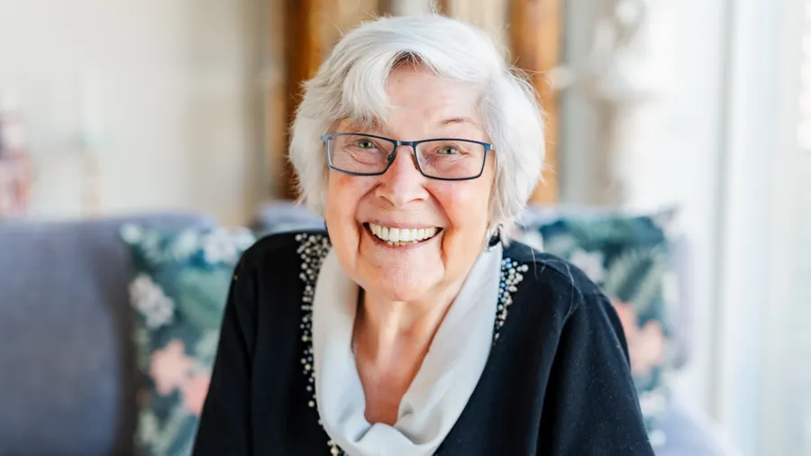 En äldre kvinna med glasögon sitter i en soffa.