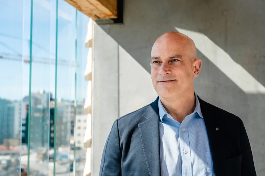 En man i kostym står framför ett fönster med byggkranar utanför.