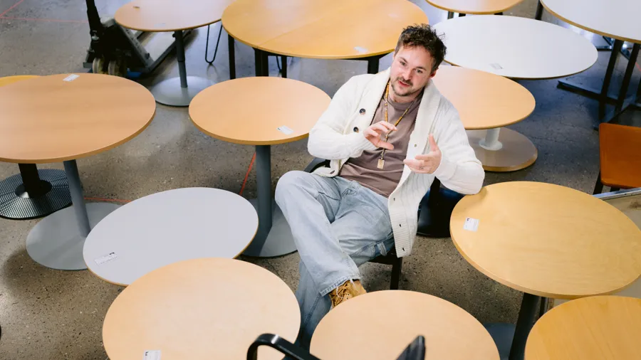 Man som sitter bland många runda träbord. 