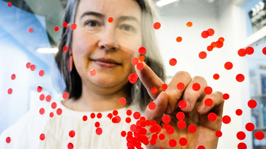 En kvinna pekar på ett rött punktmönster på en glasyta.