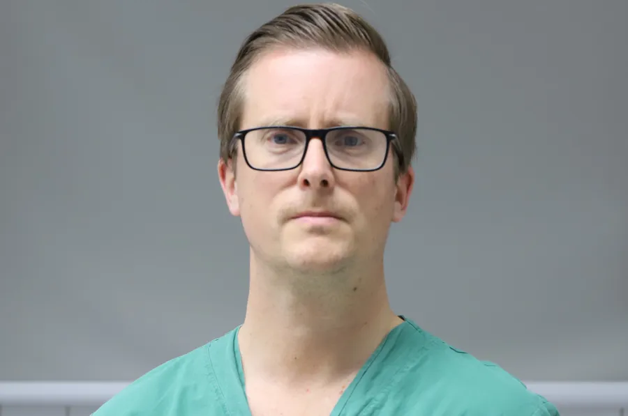 A man in a green scrub suit and glasses.