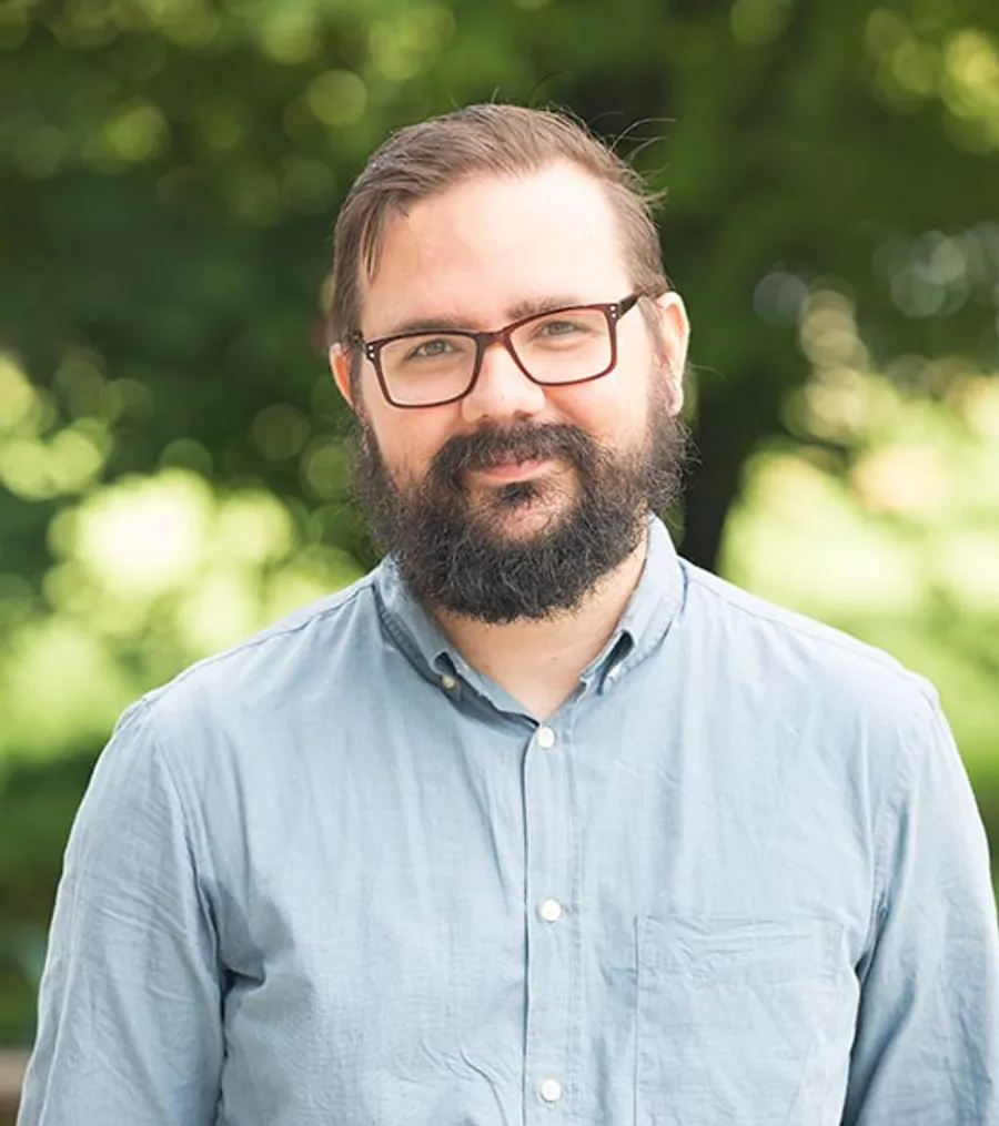 A man with a beard wearing glasses and a blue shirt.