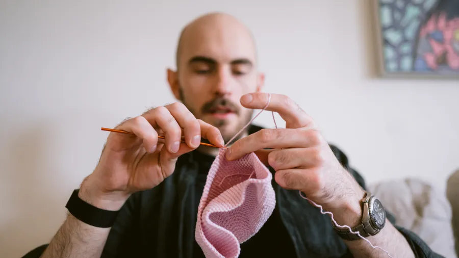 En man sitter i en soffa och virkar.