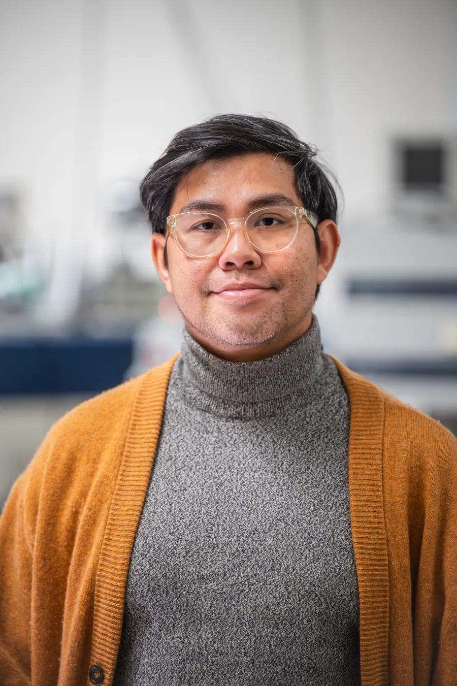 En man med glasögon och tröja står i ett labb.