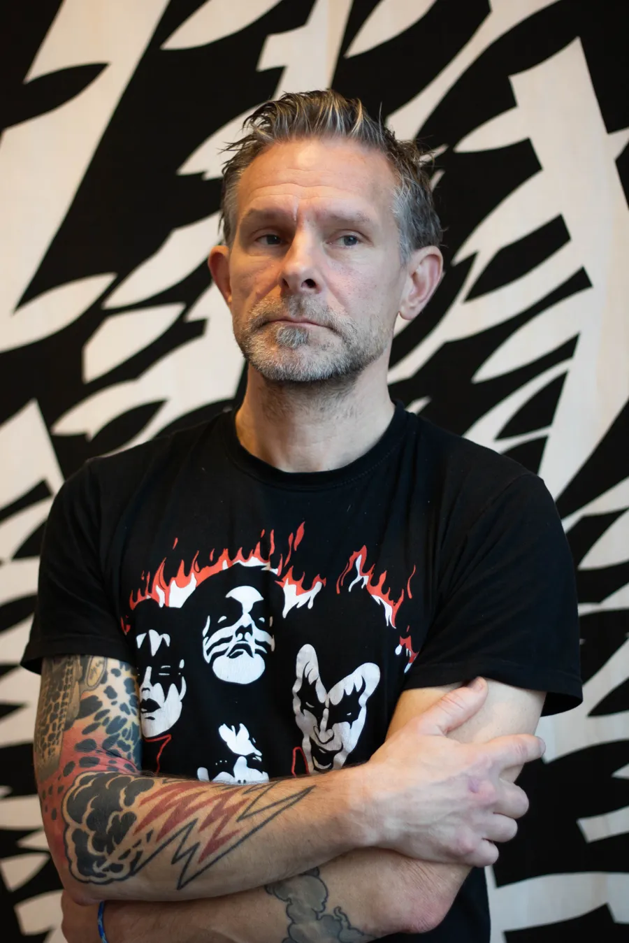 En man med tatueringar står framför en vägg.