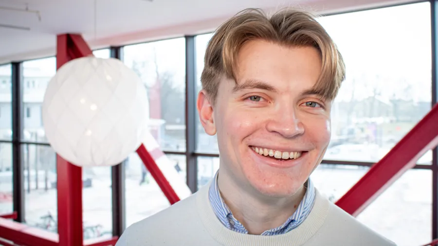 En man ler framför ett stort fönster i A-huset på Campus Valla.