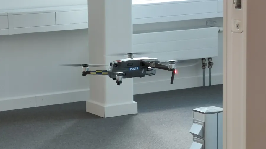 En liten polisdrönare flyger i ett tomt rum.