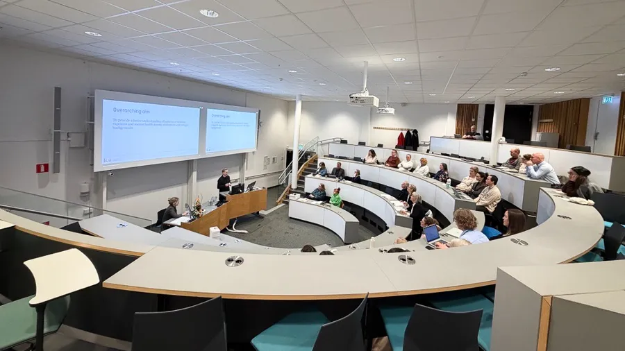 Ett rum fullt av människor som sitter vid skrivbord framför en projektorskärm.