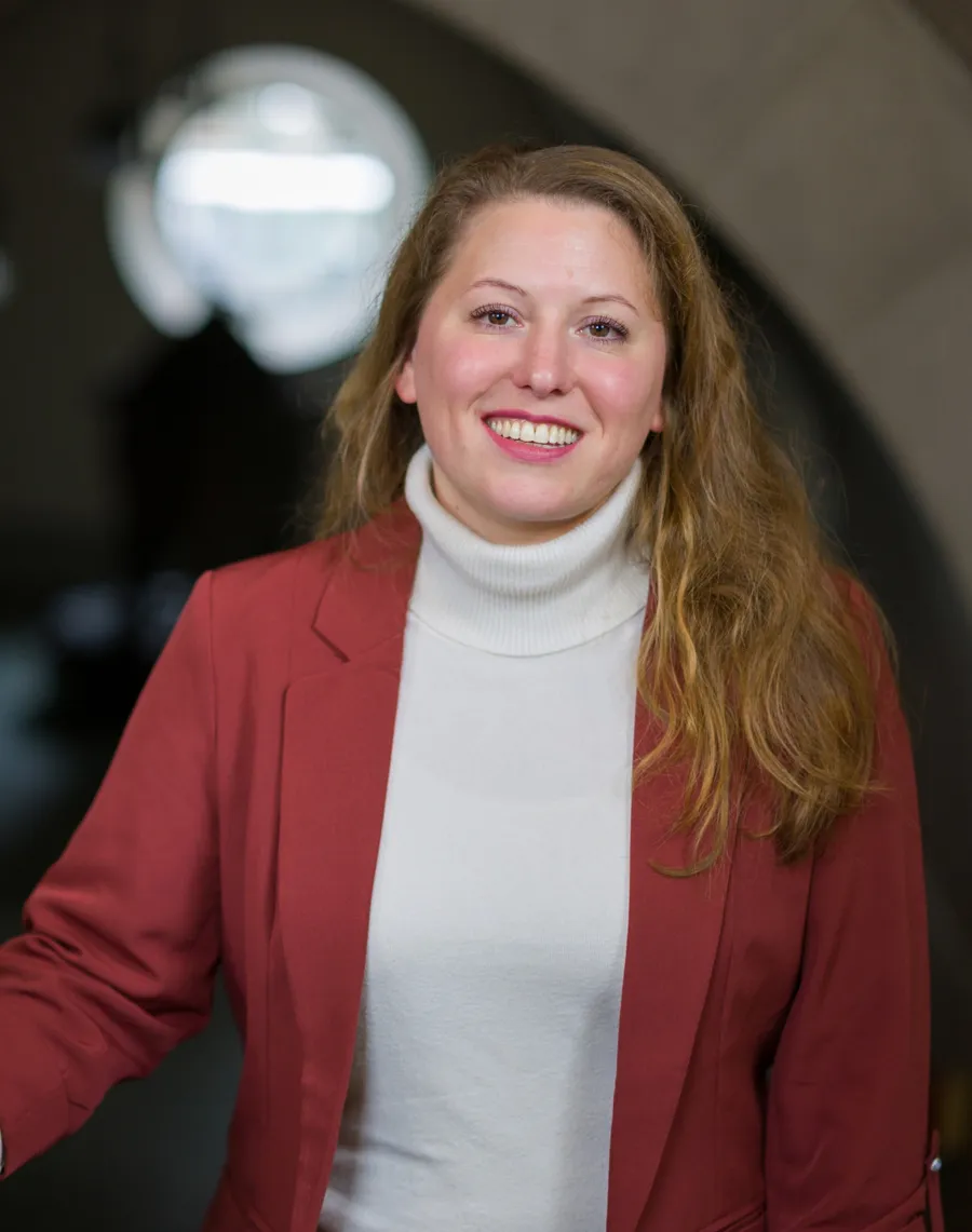 A woman wearing a red jacket and white turtle neck sweater.