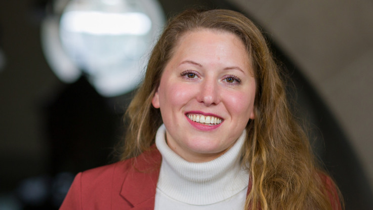 A woman wearing a red jacket and white turtle neck sweater.