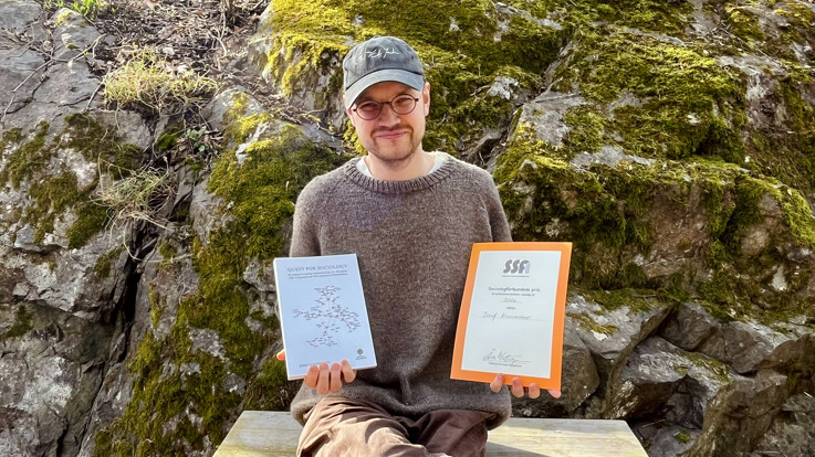 En man sitter på en bänk och håller i två plaketter.