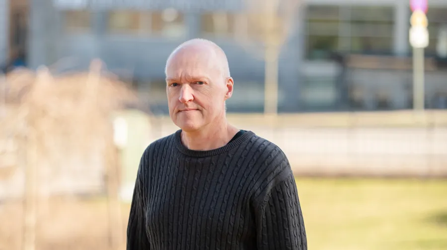 A bald man in a black sweater standing in front of a building.