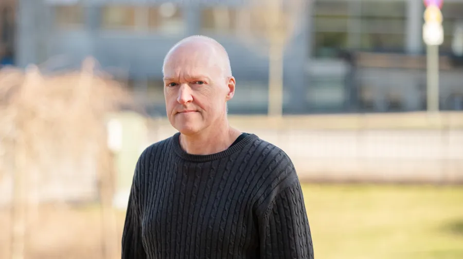 En skallig man i svart tröja står framför en byggnad.