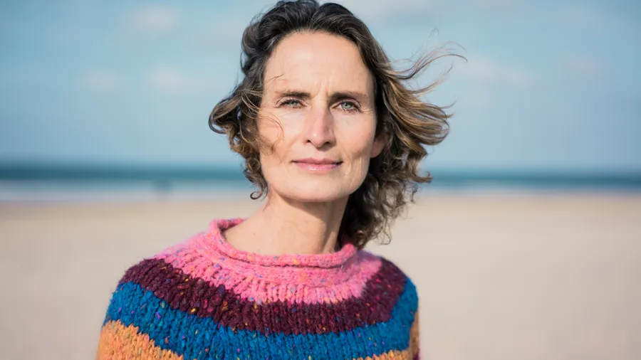 En kvinna står på en strand och bär en färgglad tröja.