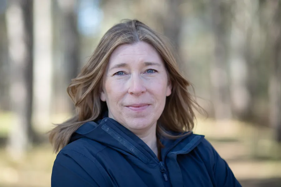 A woman standing in a forest with trees in the background.