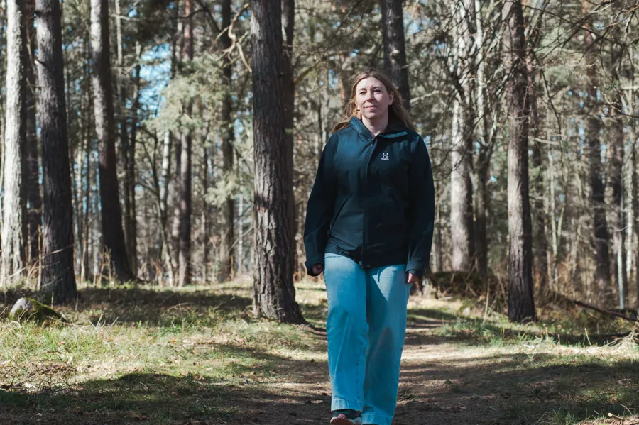 A woman in a black jacket is walking through the woods.