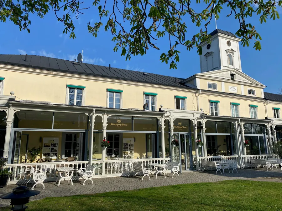 Söderköpings brunn. Byggnad med veranda, bord och bänkar framför. 