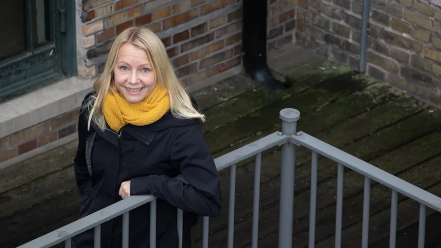 En kvinna står lutad mot ett staket och ler in i kameran.