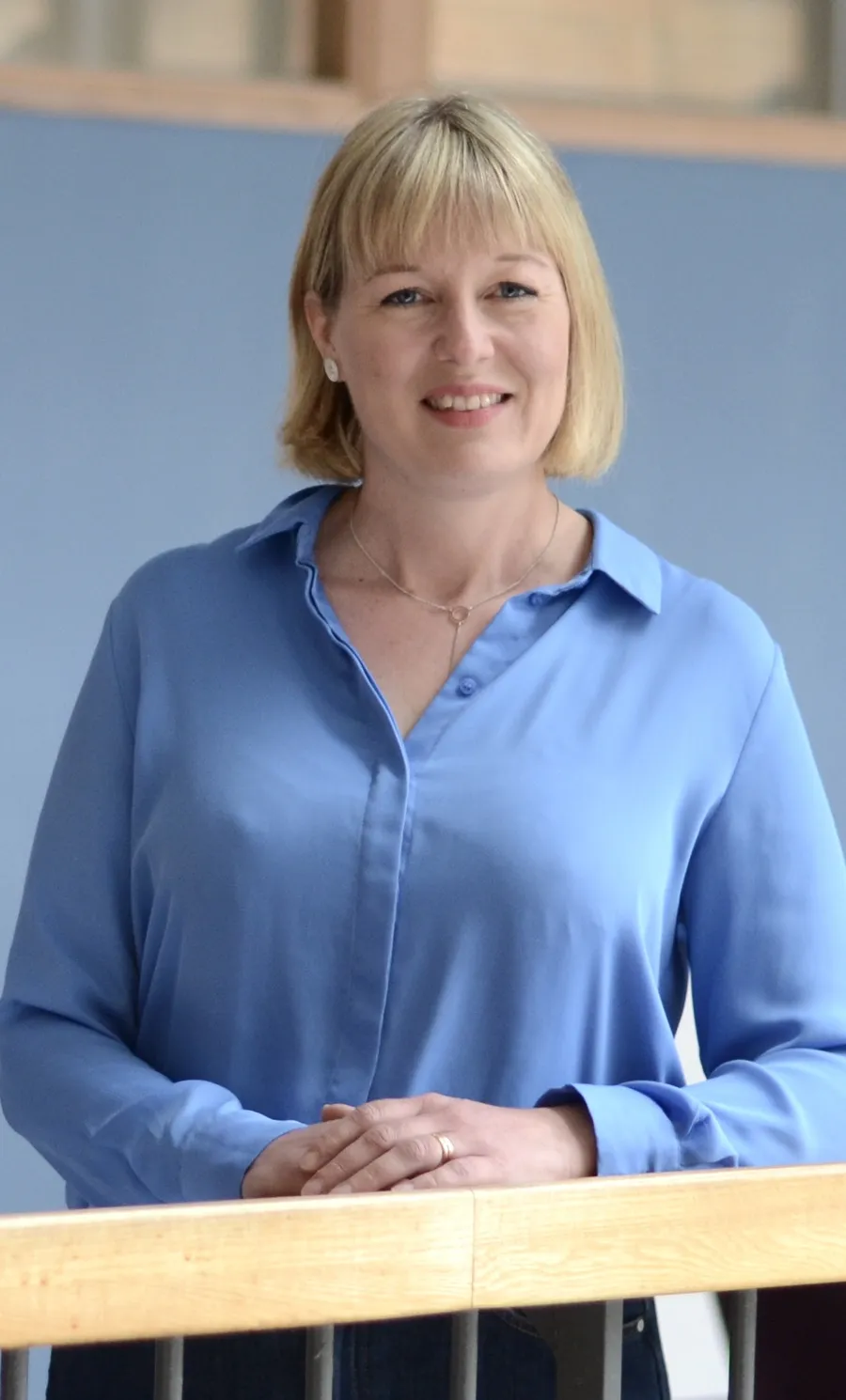 Charlotta Nordlöf lutar sig mot ett räcke och bär en blå skjorta och är fotograferad inomhus.